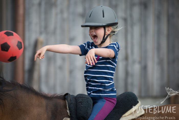 Ein Mädchen sitzt auf dem Pferd und wirft einen Ball.